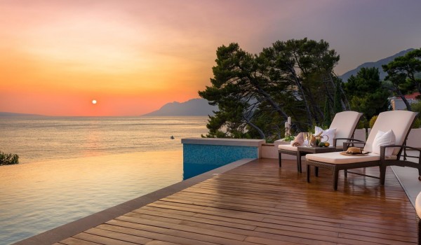 Sun deck with sunbeds next to a large heated swimming pool with a view of the sea next to the pebble beach of a modern family villa in Brela-Makarska, Croatia