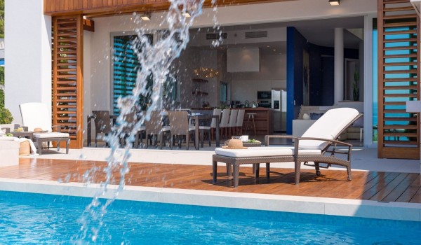 A dining table next to an open glass wall that opens onto a terrace with a heated pool and barbecue in the Brela Pride family holiday villa