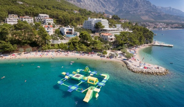 A panoramic view of the mountains and a beautiful pebble beach and a promenade by the sea with an aqua park for young people in front of the luxury villa for rent and vacation Brela Pride in 