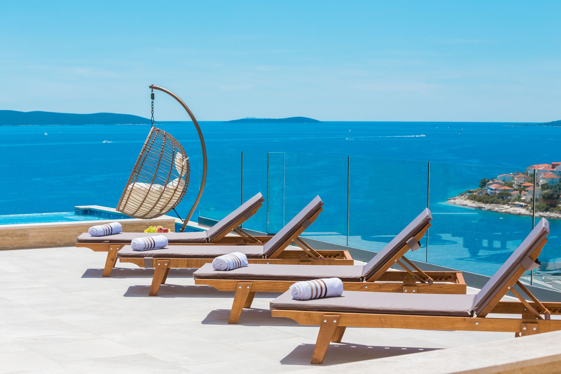 Četiri ležaljke za sunčanje te ljuljačka za sjedenje pored privatnog bazena hrvatske luksuzne vile Tresor 2 na Čiovu s panoramskim pogledom na more