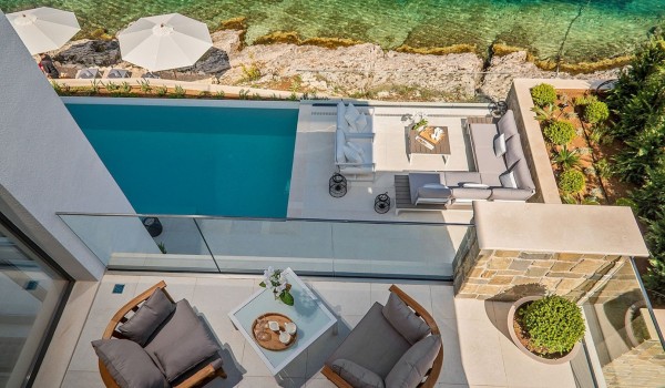 View of the exterior of the luxury villa Korcula Prestige with an outdoor terrace with a pool and seating and a balcony with armchairs and a table and a view of the sea
