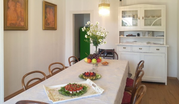 Dining table decorated with fresh flowers and fresh fruit and equipped with 8 wooden chairs and a wooden chest of drawers