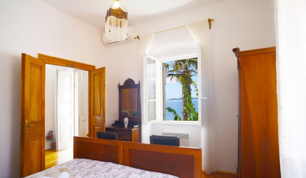 A bedroom with a double bed, a wooden wardrobe and a window with a view of the sea in the villa Beach House Orebic with pool