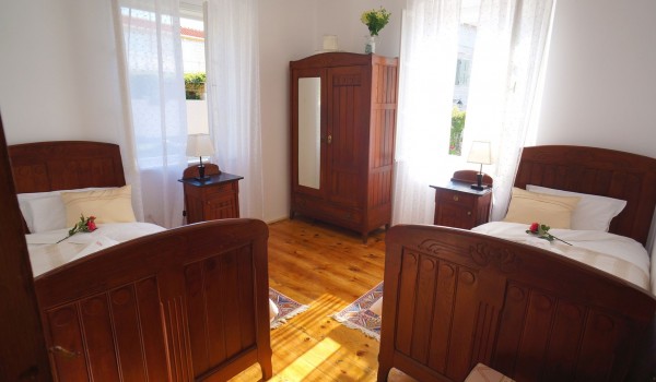 A bedroom with two single beds and a wooden wardrobe and wooden chests of drawers