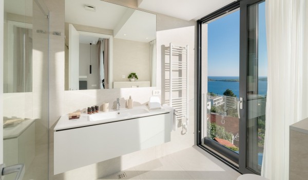Bathroom area with the sink and the big mirror above and with the floor-to-ceiling glass window overlooking the sea