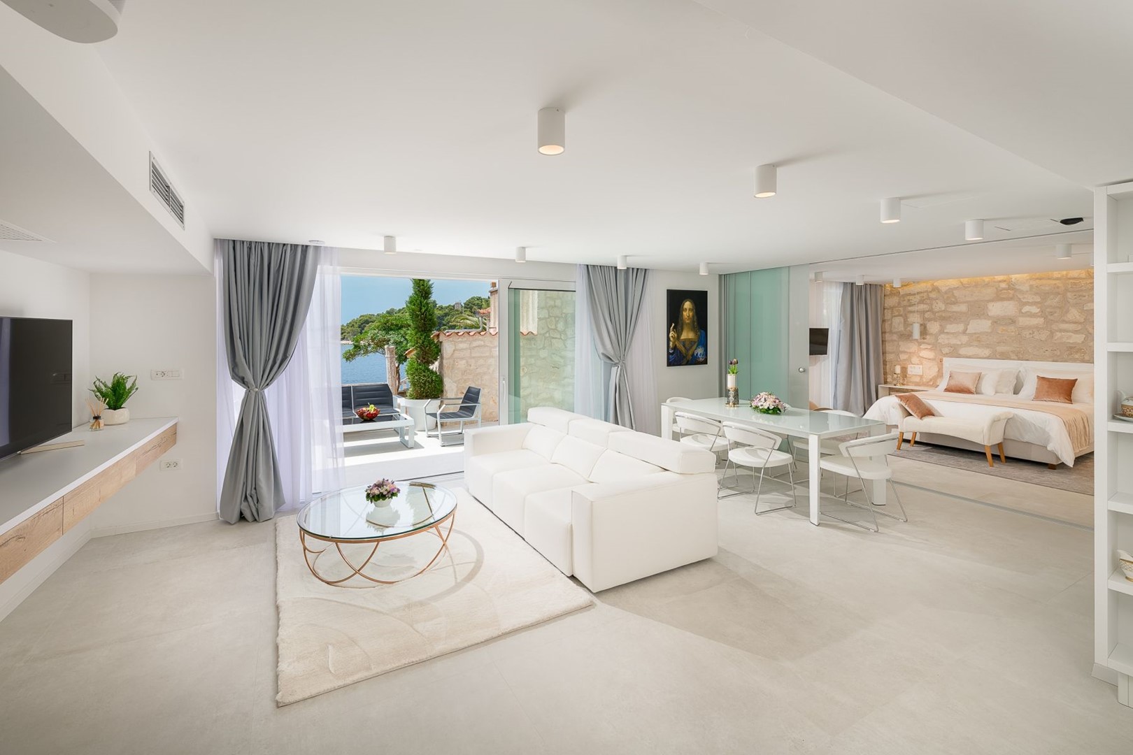The interior of a Croatia luxury villa with a double bed, a sofa set with a coffee table, an LCD TV and an exit to the outdoor terrace in the luxury villa Gariful on Hvar