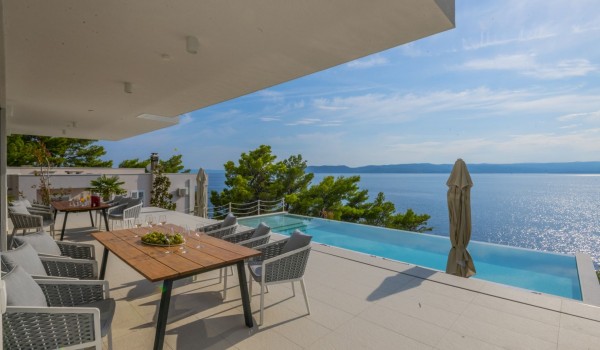 View of the dining table, private heated swimming pool and the sea from the outdoor terrace of the luxurious holiday villa Glorious Brela in Brela