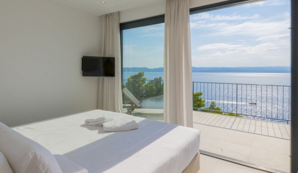 A bedroom with a double bed, an LCD TV and a private balcony with a view of the sea in the luxurious villa Glorious Brela in Brela