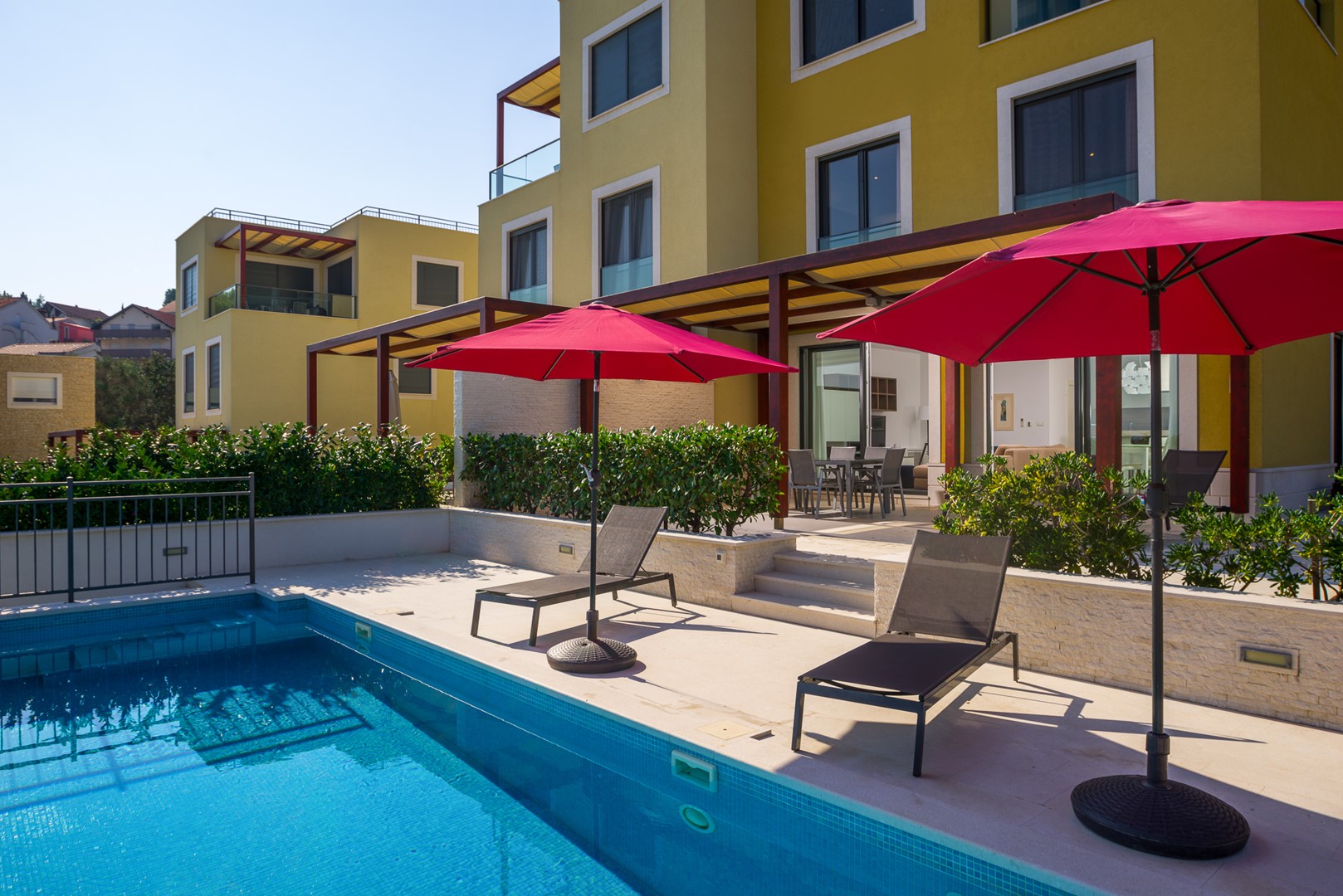 Liegestühle und Sonnenschirme am Pool einer kroatische Luxus-Ferienvilla am Strand von Ciovo
