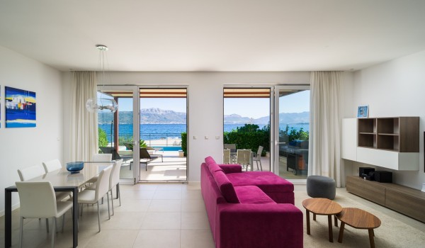 Dining table and comfortable sofa in a living room with a direct entrance to the terrace of a luxury vacation villa for families with kids