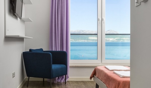 View of a double bed and armchair in a bedroom of a luxury beachfront villa for vacation and rent in Ciovo