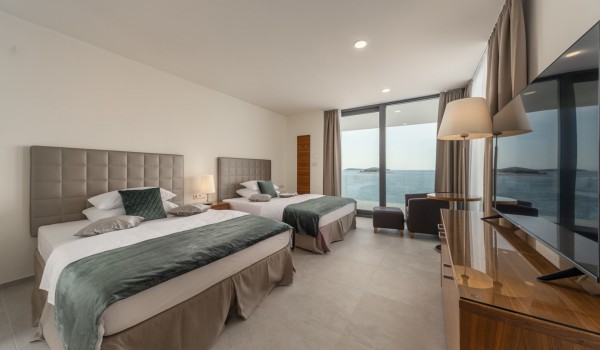 A bedroom with two double beds, an LCD TV, a sitting area and a view of the sea in the luxurious holiday villa Supreme Rogoznica 2 in Rogoznica