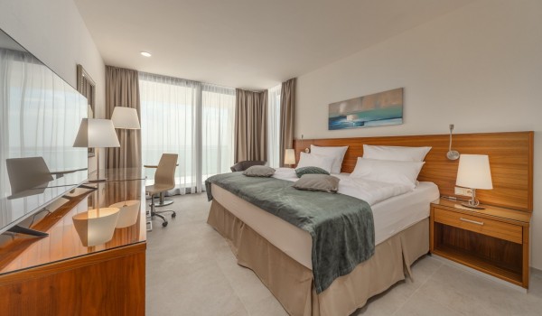 A double bed, an LCD TV and a sitting and rest area with an armchair and a coffee table in the bedroom in a luxury villa for a family holiday in Rogoznica