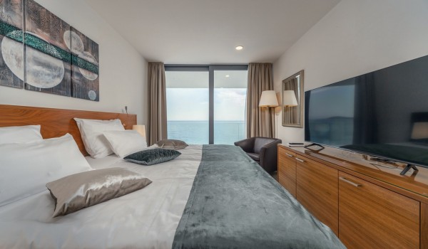 Comfortable double bed, LCD TV and armchair in the bedroom with a view of the sea in a luxury villa with a private pool in Rogoznica