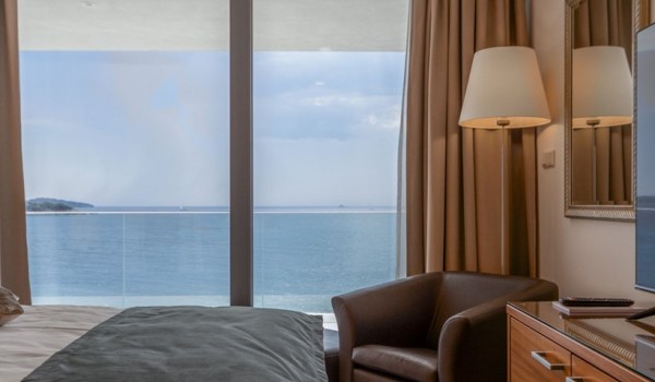 A bedroom with a double bed, an armchair and its own exit to the balcony with a view of the sea in the luxury villa Supreme Rogoznica 2 in Rogoznica