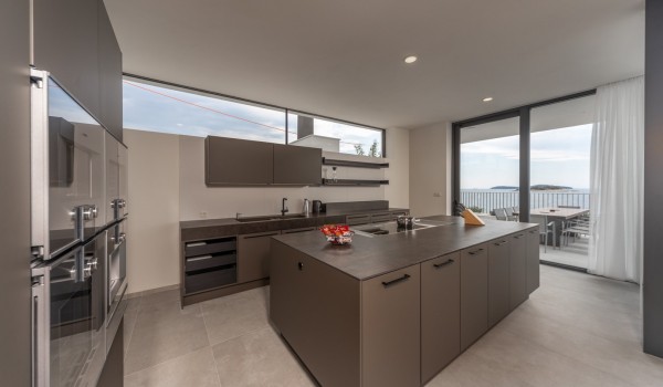 Kitchen equipped with oven, stove, coffee machine and kitchen island and exit to the outdoor terrace of the luxury holiday villa in Rogoznica