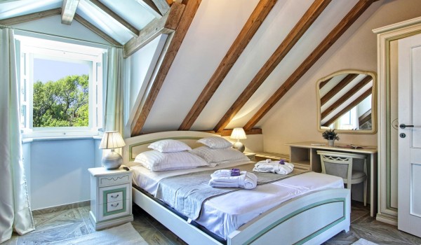 Sunny bedroom with a king size bed, LCD TV and a stone wall in the attic of the private home rental Cavtat Iliria with a garden and a jacuzzi