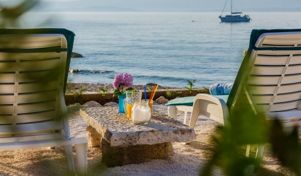 Sun beds and little stone table on the sandy courtyard overlooking the beach in the beachfront holiday villa with private parking