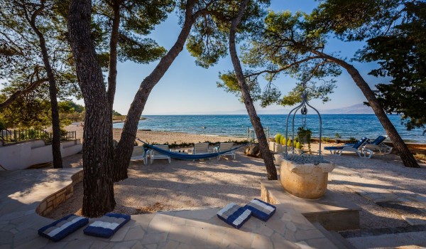 Sandy and pebbly courtyard with deck chairs and hammock of the traditional stone house for family vacation by the sea on Brac island