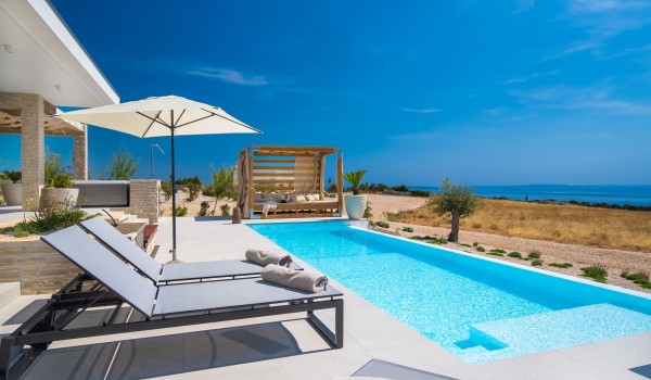 View of the large swimming pool with deckchairs for rest and relaxation in the famous luxury air-conditioned villa for rent Summer Dream Privacy Novalja surrounded by greenery on the island o