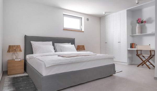 Interior of a modern bedroom with a double bed, sitting area and SAT TV of a family villa for rent on the island of Pag with a view of the sea and the beach