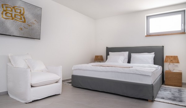 A spacious bedroom with a king-size bed, a lounge chair and a SMART TV. Villas for vacation and rental with a swimming pool on the island of Pag with a chef service on request