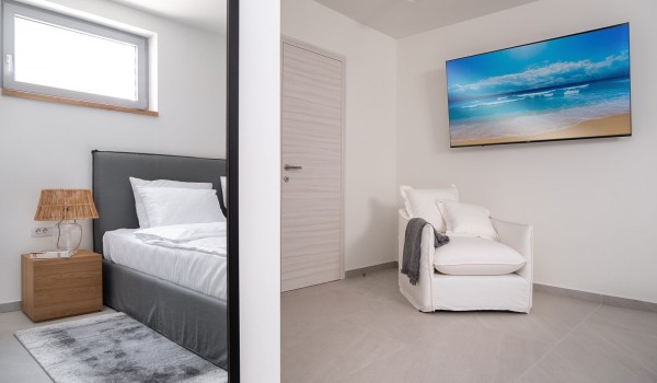 A modernly decorated bedroom with a king size bed, an armchair and SAT TV in a villa for rent with a swimming pool Summer Dream Privacy Novalja next to the beach on the island of Pag