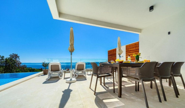 Outdoor terrace with table, chairs and comfortable sunbeds by the swimming pool of a luxurious Croatian holiday villa