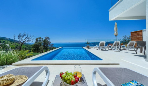 Outdoor terrace with comfortable deckchairs next to the heated swimming pool on the property of a private holiday villa