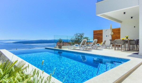 Outdoor terrace with table, chairs and comfortable sunbeds by the swimming pool of a luxurious Croatian holiday villa