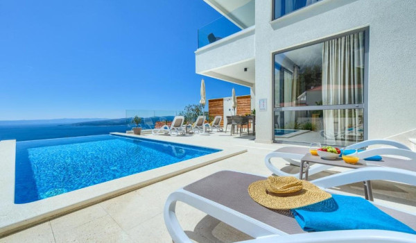 Outdoor terrace with table, chairs and comfortable sunbeds by the swimming pool of a luxurious Croatian holiday villa