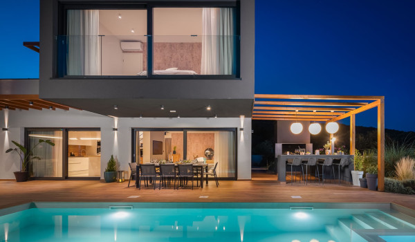 Outdoor dining table with chairs next to the private pool in front of the modern family villa for rent Indigo in Razanj and a BBQ with dining area