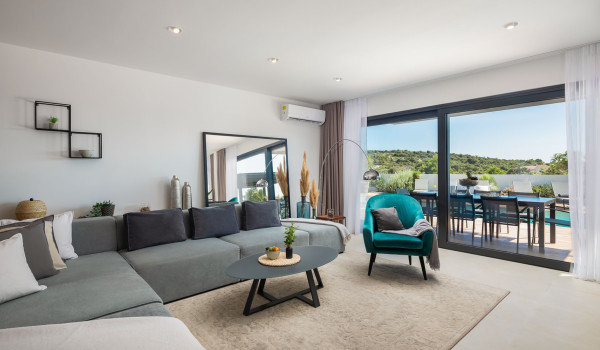 Modernly decorated living room with air condition, angular sofa and a sophisticated armchair in the Dalmatian rental home in Razanj