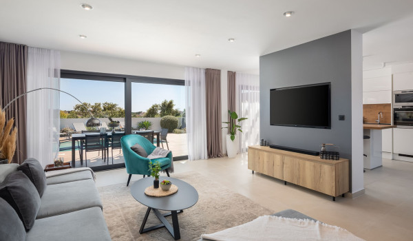 Modern living room with an angular sofa, armchair and SAT TV next to the access to the patio with pool and sun loungers