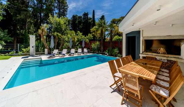 Dining table with chairs for 10 people and a wood-burning fireplace next to the pool with sunloungers and parasols in front of the modern villa Velvet Bourbon Split