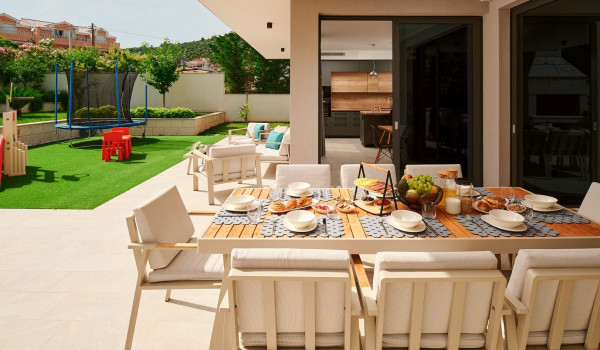 Roofed part of the patio with an outdoor wooden dining table and chairs and a children's playground in the garden