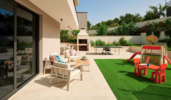 Seating corner and children's playground in the fenced private garden of the luxury villa Thalia with an indoor pool