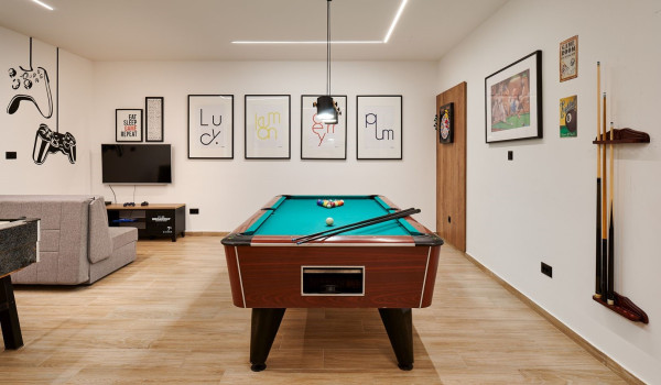 Pool table, darts and gaming corner with sofa, TV and gaming console in the game room of the modern villa Thalia in Marina