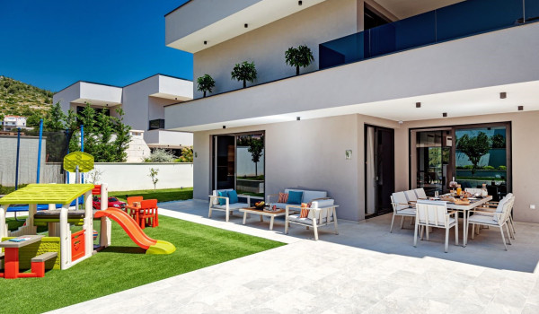 Fenced private yard with a children's playground and seating area on the property of the modern family villa Thalia