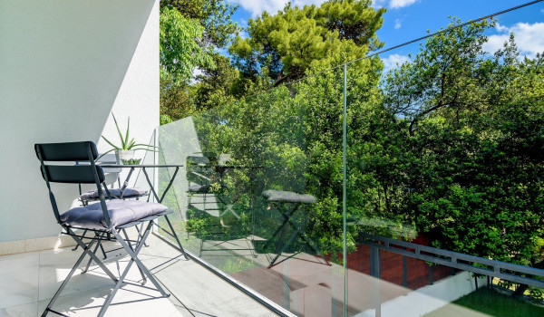 Seating area on the balcony surrounded by glass fence and view of the greenery and the forest