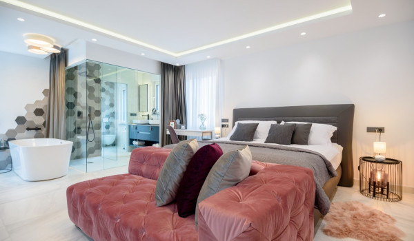 Comfortable king size bed with seating area in the modern bedroom with bathtub and en suite bathroom
