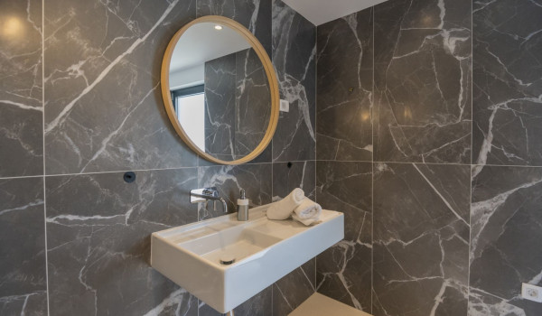 A large round mirror and a sink in a modern bathroom in a luxury villa with a view of the sea in Brela