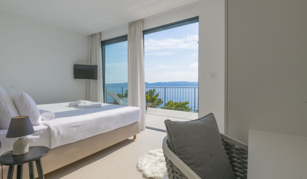 A bedroom with a double bed, a desk with a chair and its own exit to the balcony in a luxury villa for vacation and rent in Brela